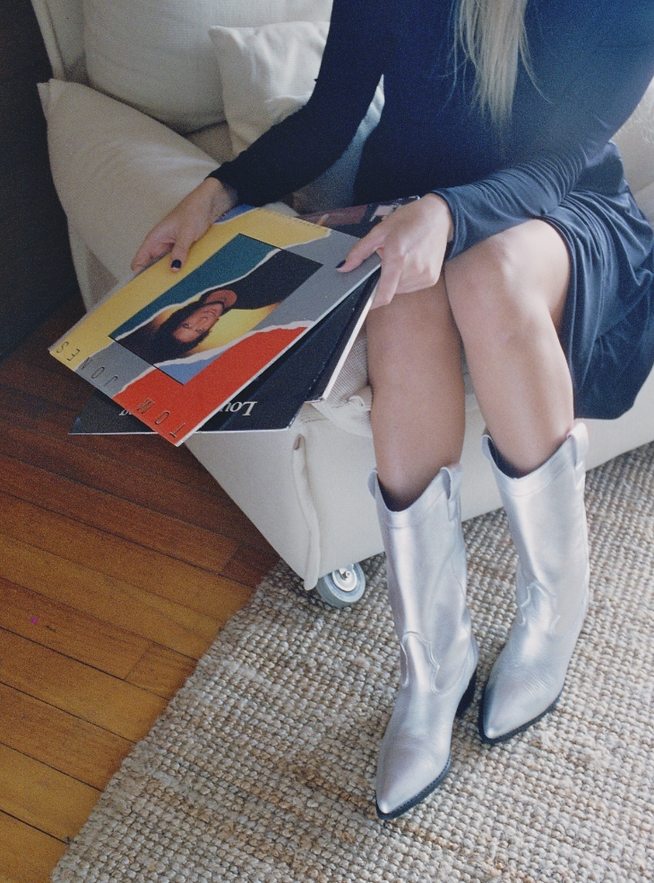 Chica sentada en un sofá, con botas y varios discos de vinilo